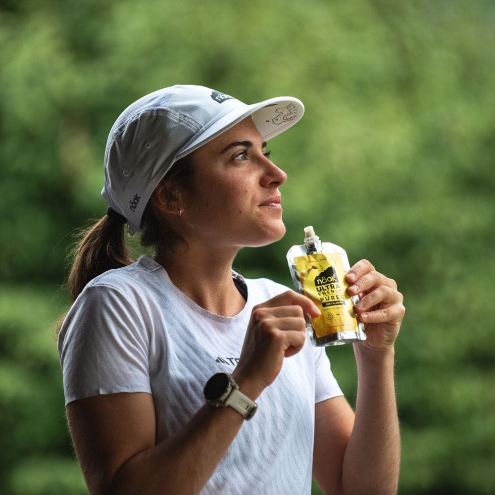 Woman holding a naak ultra energy puree banana pear with a blurred green background